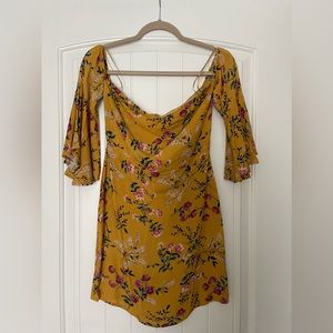 Short over the shoulder dress. Color is mustard with flowers